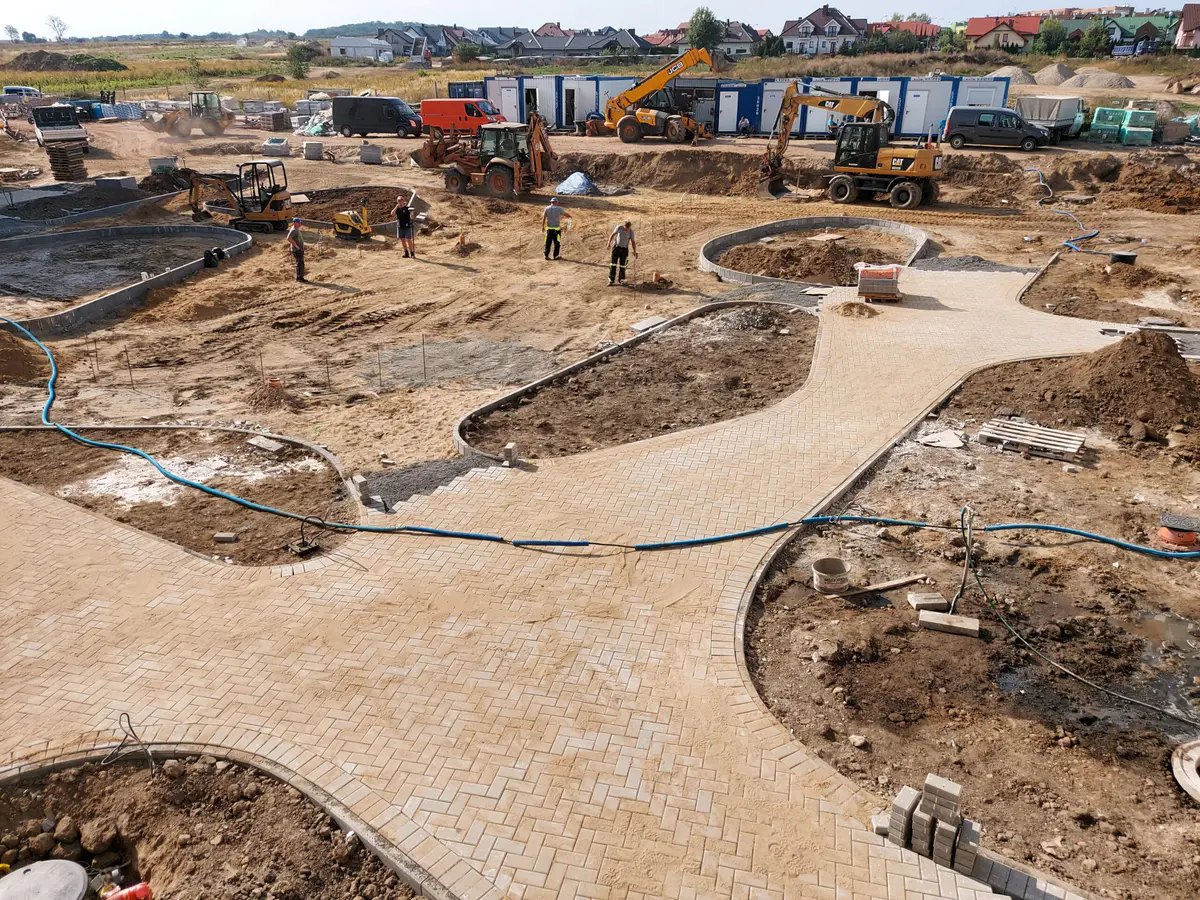 Duży plac budowy – alejki z kostki brukowej, maszyny i ekipy wykonawców
